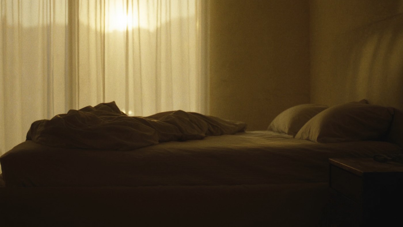 Empty bed with golden sunrise light through the curtains at dawn