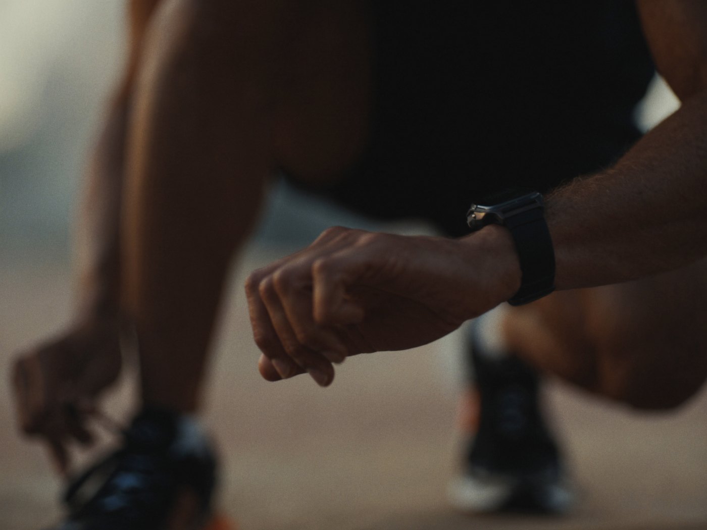 Athlete lacing up running shoes and checking a smartwatch before a morning workout