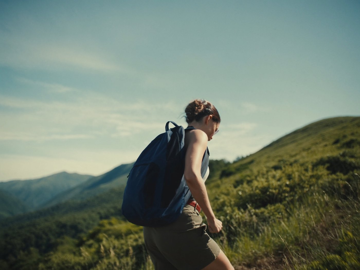 Hiker climbing a scenic mountain trail with a small backpack under open sky